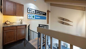 A staircase with a wooden handrail, a wall-mounted sign indicating directions to Storm Peak Express and Sundial, and a kitchen area with wooden cabinets and a clock. - Lofted Mountain Lookout (Steamboat Springs)