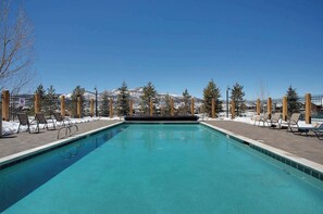 A rectangular swimming pool with clear blue water, surrounded by a wooden deck and lounge chairs. - Lofted Mountain Lookout (Steamboat Springs)