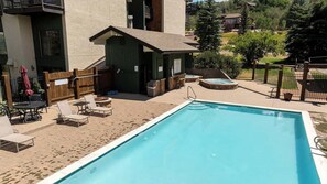 A swimming pool with lounge chairs and a hot tub, surrounded by a wooden fence and a building with a balcony. - Lofted Mountain Lookout (Steamboat Springs)