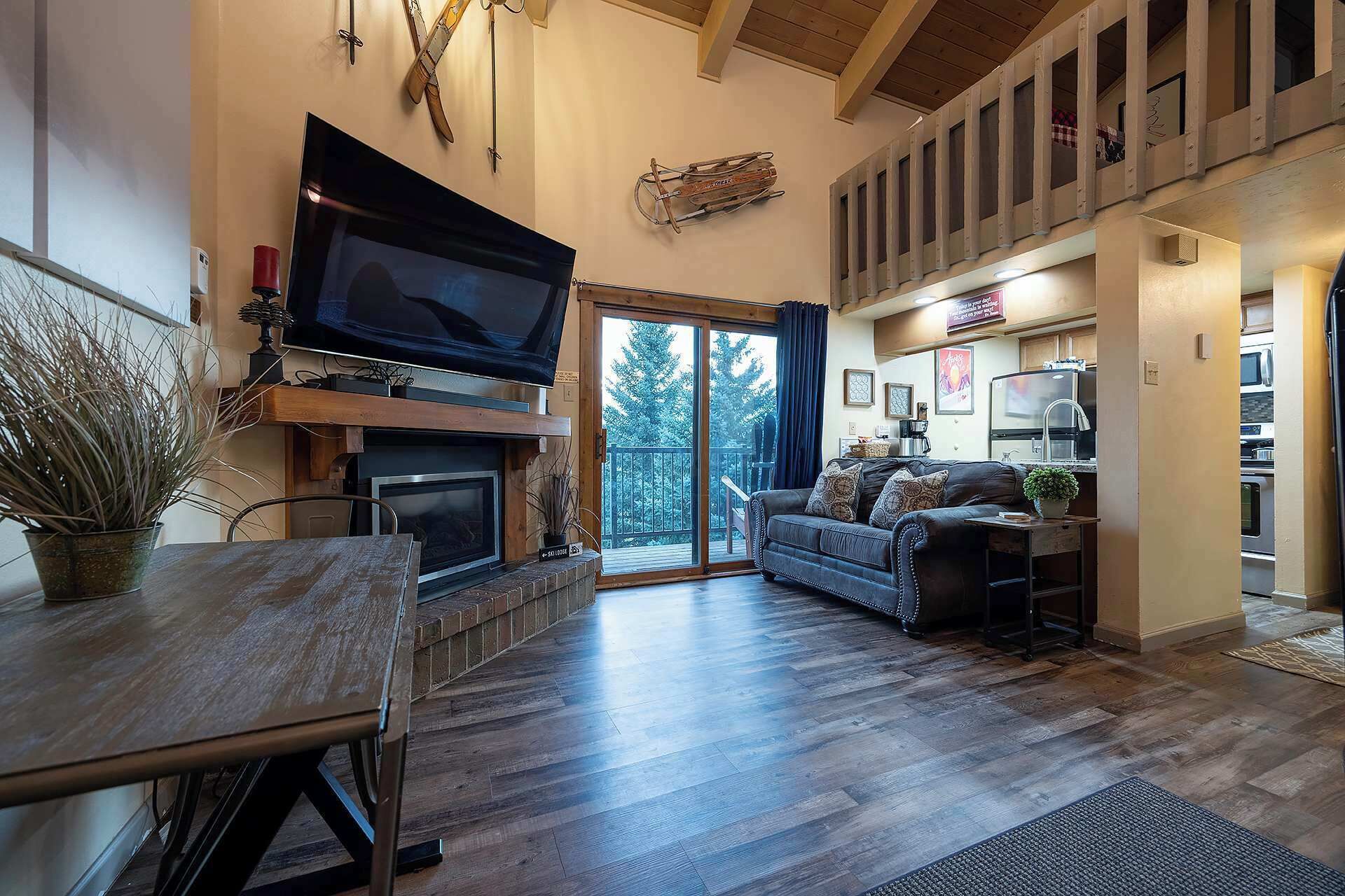 A cozy living room with a fireplace, a flat-screen TV, and a sliding glass door leading to a balcony.