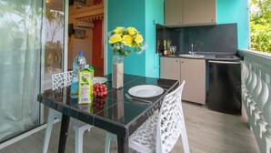 A dining area with a glass table, white chairs, a vase with yellow flowers, a bottle of water, and a carton of juice. - Rêve Bleu 10 - Clim - Proche plage (LE DIAMANT)