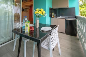 A dining area with a glass table, white chairs, a vase with yellow flowers, a bottle of water, and a carton of juice. - Rêve Bleu 10 - Clim - Proche plage (LE DIAMANT)