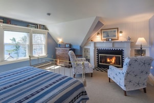 Un dormitorio con una cama, dos sillones, una chimenea y una ventana con vistas al agua.