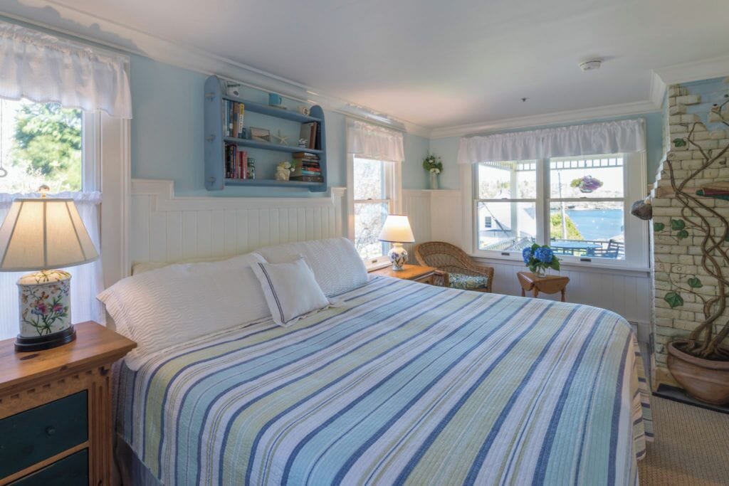 A bedroom with a bed, a nightstand, a chair, a window with a view, and a bookshelf.