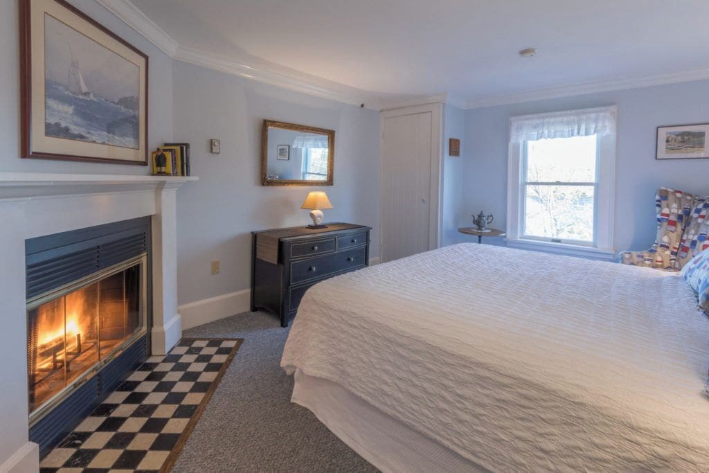 A bedroom with a fireplace, a bed, a dresser, and a window.