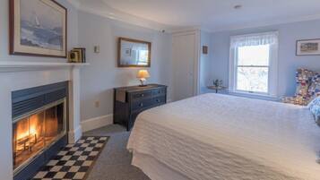 A bedroom with a fireplace, a bed, a dresser, and a window.