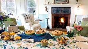 A cozy living room with a fireplace, a dining table set with food, and comfortable seating. - Five Gables Inn (East Boothbay)