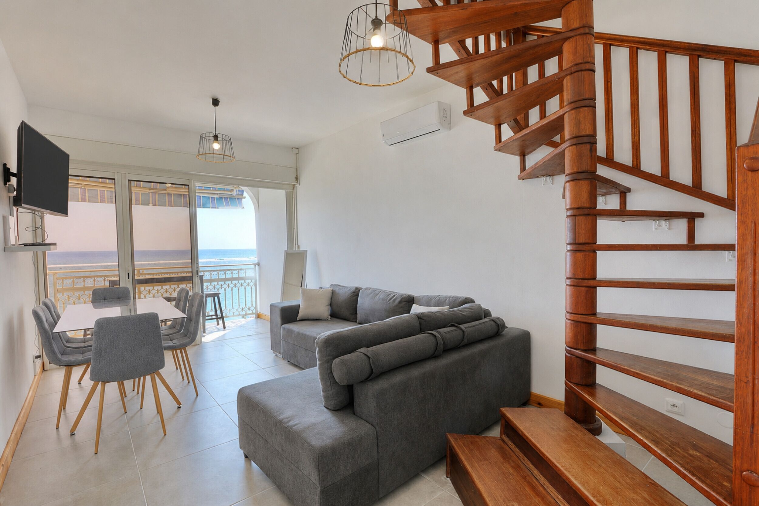 Ein modernes Wohnzimmer mit einem grauen Ecksofa, einer Holztreppe und einem Balkon mit Blick.