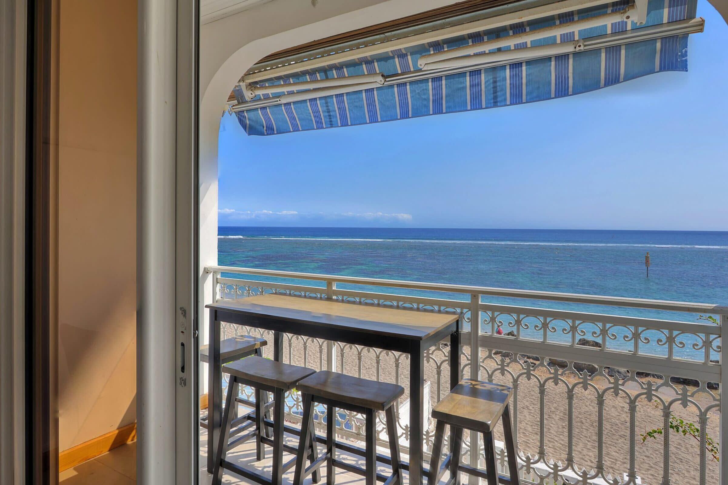 A balcony with a view of the ocean, a table, and two bar stools.