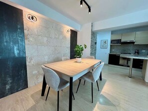 Un comedor moderno con una mesa y sillas de madera, una planta en maceta y una cocina al fondo.