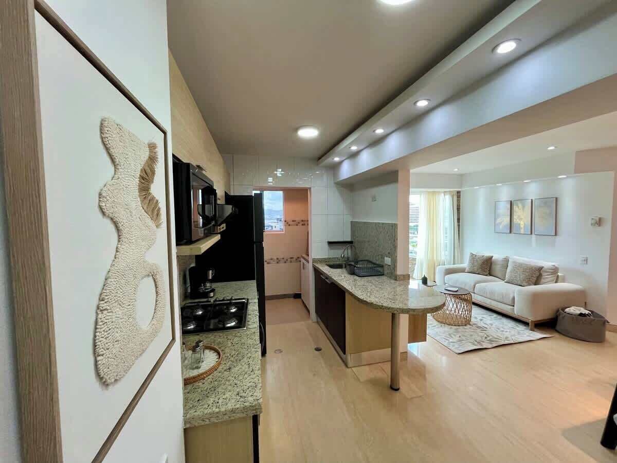 Una cocina moderna con una isla central, un área de comedor con sofá y una sala de estar con diván.