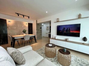 A modern living room with a sofa, a dining area, and a TV mounted on the wall. - Vistas Increibles y Confort en El Rosal (Caracas)