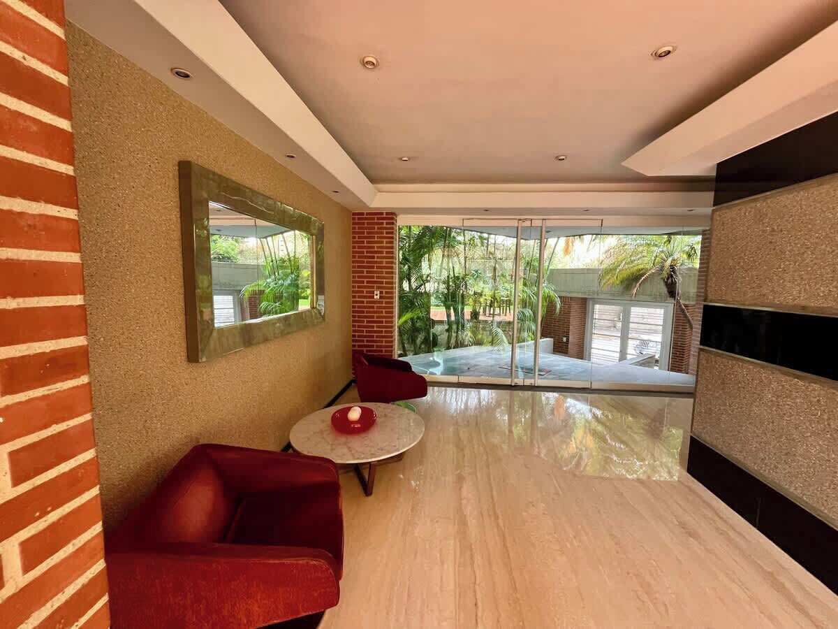 Un interior moderno con un sofá rojo, una mesita redonda y una puerta de vidrio que da a un área exterior.