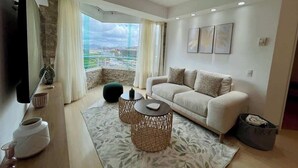 A modern living room with a sofa, two round coffee tables, a flat-screen TV, and a large window offering a city view. - Vistas Increibles y Confort en El Rosal (Caracas)