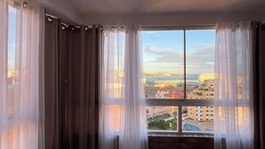Una habitación con un ventanal grande, cortinas y vista a un paisaje urbano.
