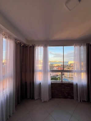 Ein Zimmer mit großem Fenster, Vorhängen und Blick auf eine Stadtlandschaft.