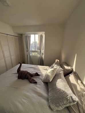 Ein Schlafzimmer mit Bett, einem fenster mit Vorhängen und Blick auf Gebäude.