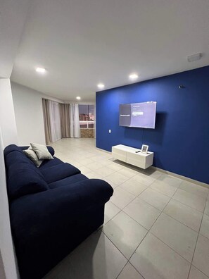 Ein modernes Wohnzimmer mit einem dunkelblauen Sofa, einer weißen TV-Konsole und einem großen Fenster mit Vorhängen.