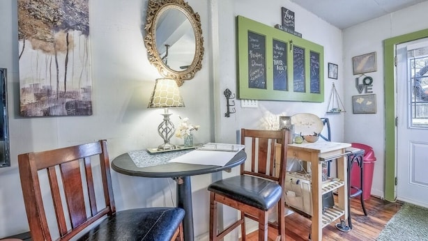 Una stanza con un tavolo rotondo, due sedie di legno, uno specchio e un elemento decorativo appeso al muro con cornice verde.