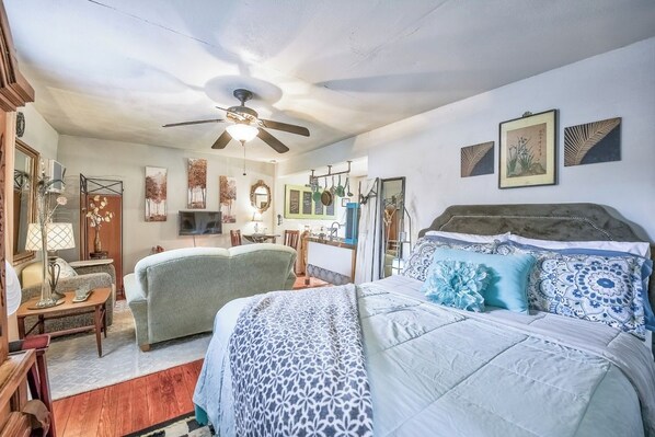 A bedroom with a bed, a ceiling fan, a TV, and artwork on the walls.