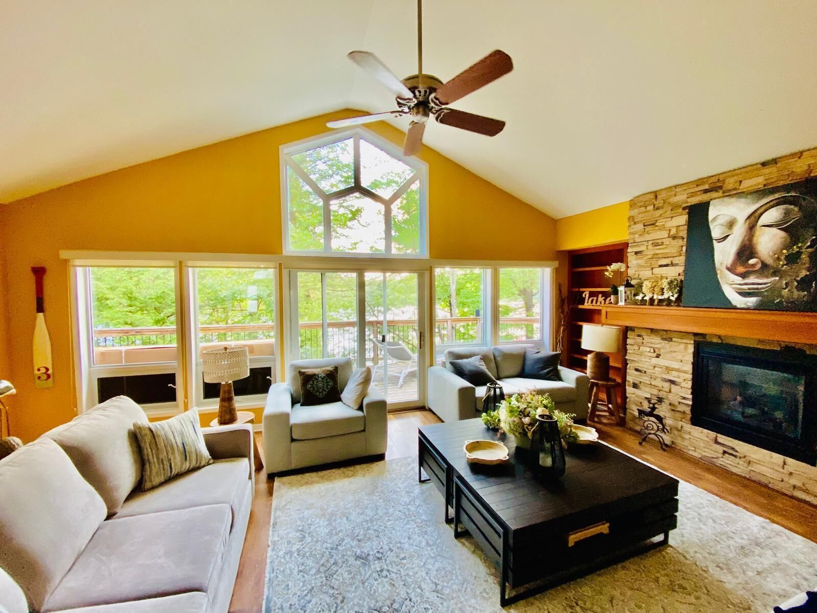 A spacious living room with a high ceiling, a fireplace, and a large window overlooking a deck.