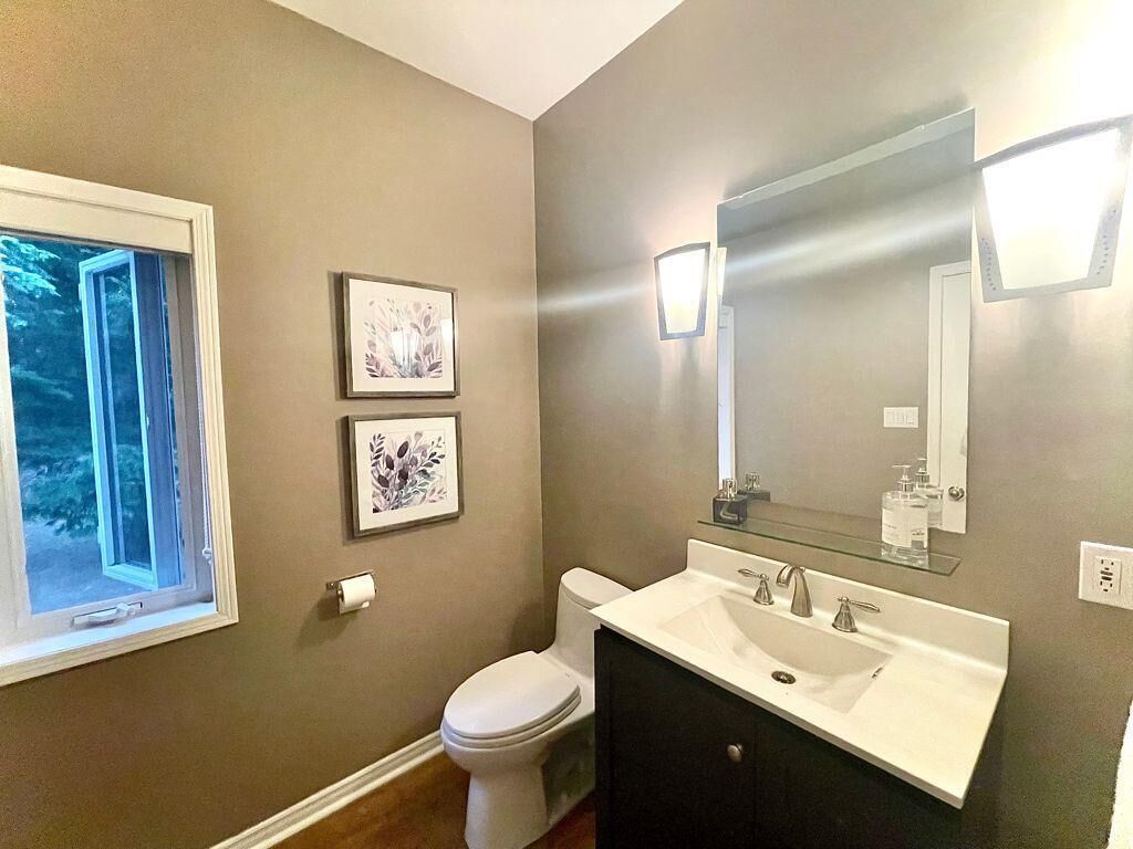A bathroom with a toilet, sink, and mirror. There are two framed pictures on the wall.