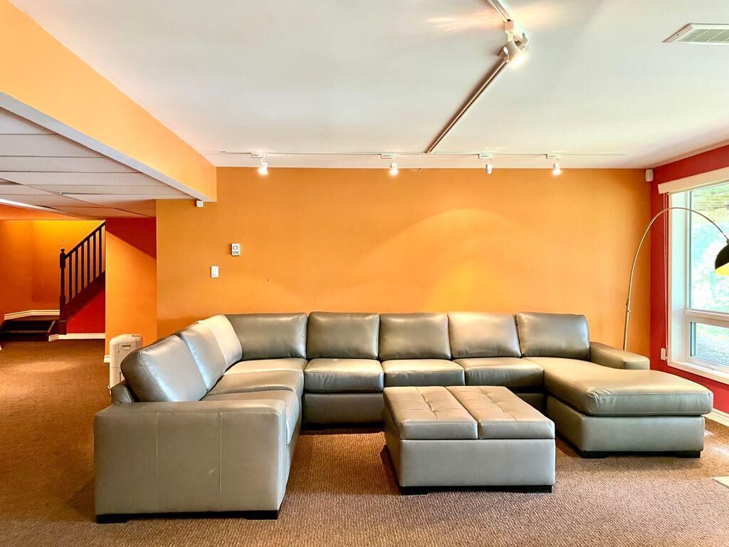 Un grand canapé d’angle en forme de L dans une pièce aux murs orange et au sol recouvert d’une moquette.