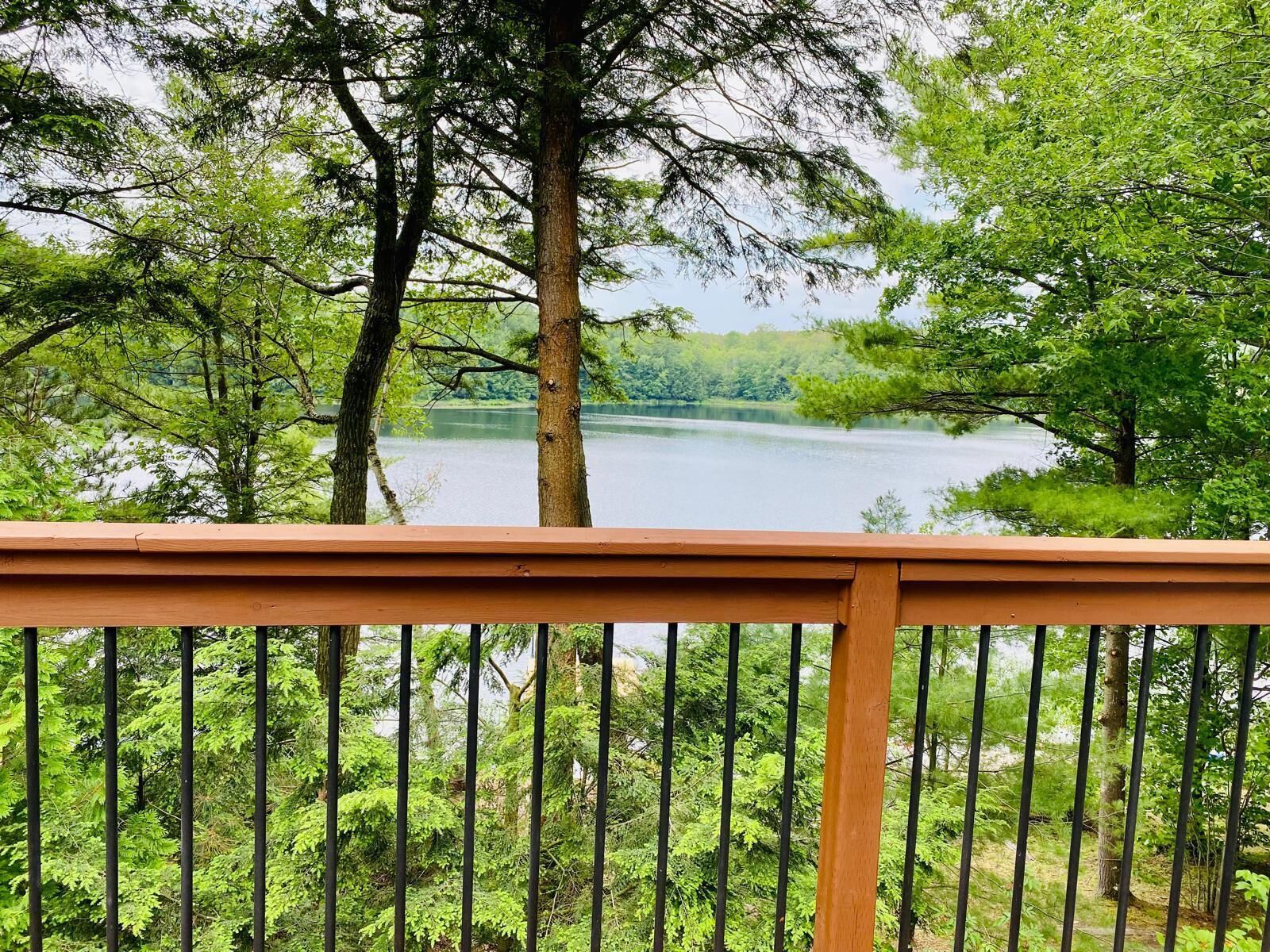 Une terrasse en bois donnant sur un lac, lui-même entouré d’arbres.