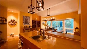 Une cuisine dotée d’un grand îlot central, de luminaires suspendus et offrant une vue sur l’extérieur grâce à de grandes fenêtres.