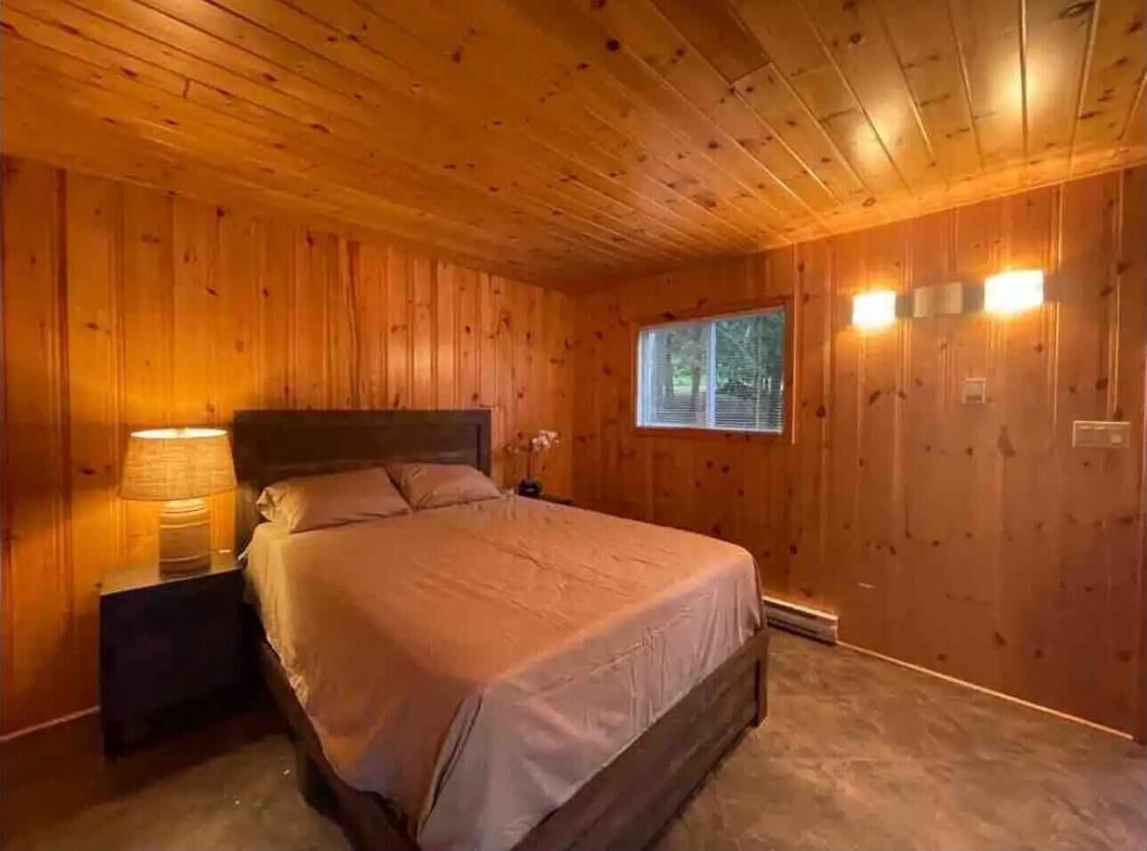 A wooden-paneled bedroom with a bed, nightstands, and wall-mounted lights.