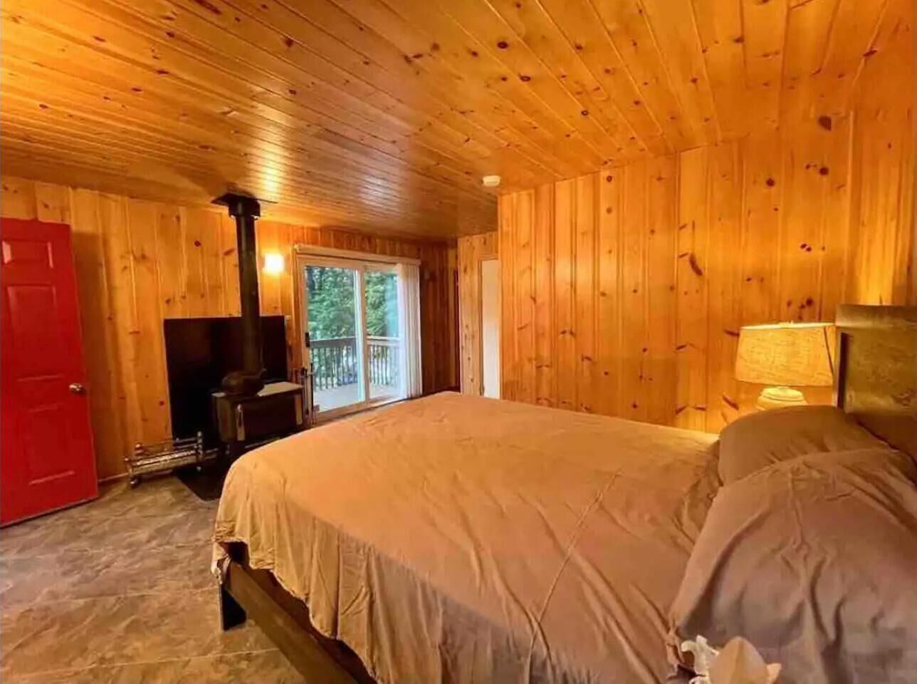 Une chambre dans une cabane en bois, avec un lit, une cheminée et une vue sur l’extérieur.