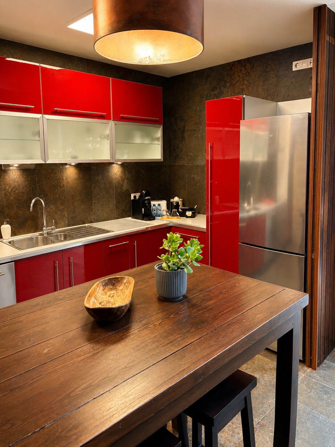 Una cocina moderna con armarios rojos, un refrigerador de acero inoxidable, una mesa de madera y una planta en maceta.