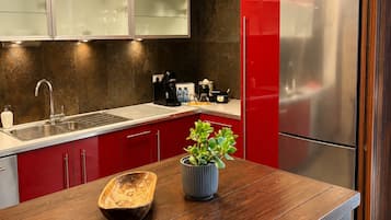 Una cocina moderna con armarios rojos, un refrigerador de acero inoxidable, una mesa de madera y una planta en maceta.