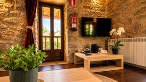 A room with a stone wall, a wooden door, a television, a coffee machine, a telephone, and a potted plant.