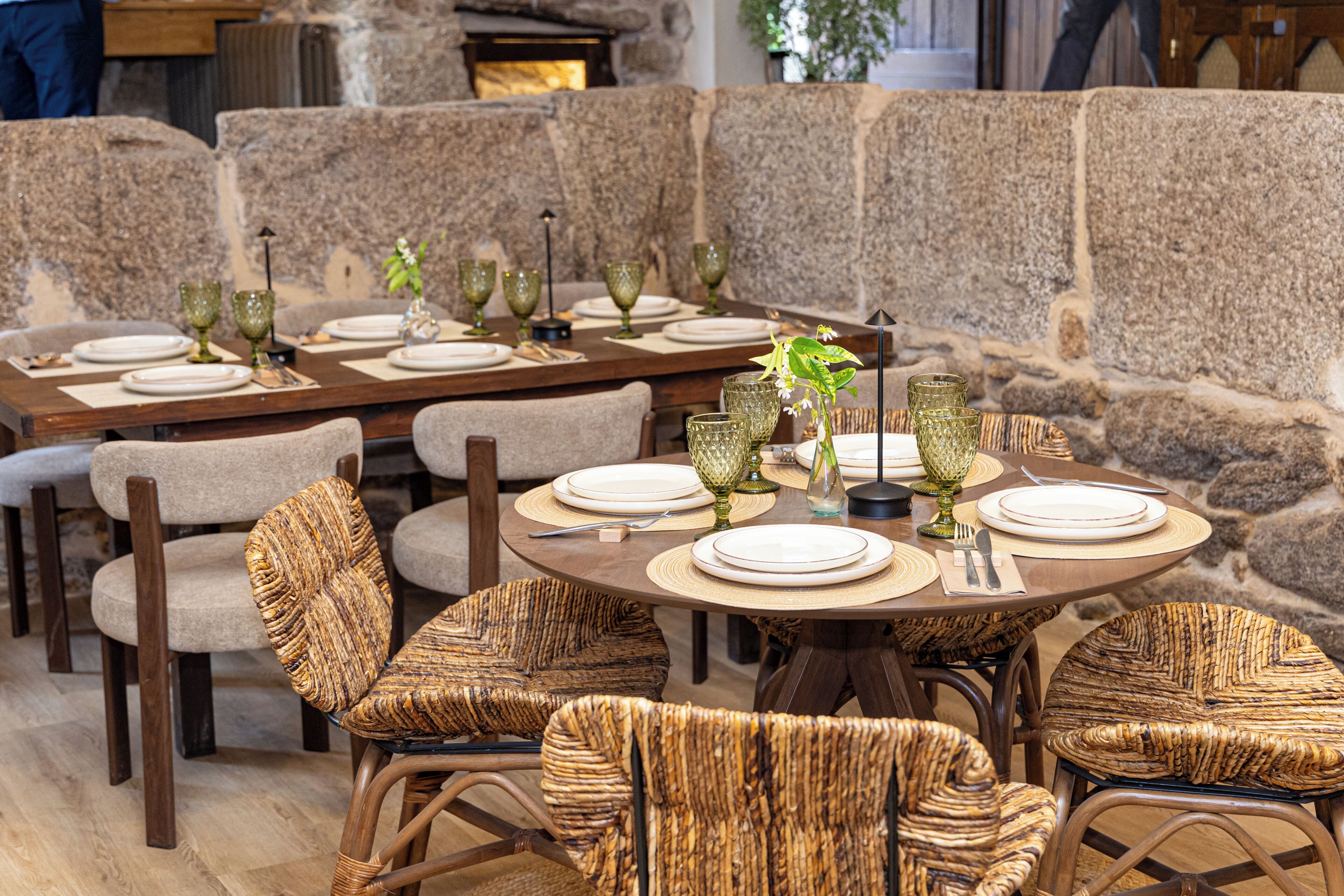 A restaurant with round tables set for dining, wicker chairs, and stone walls.