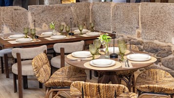 A restaurant with round tables set for dining, wicker chairs, and stone walls.