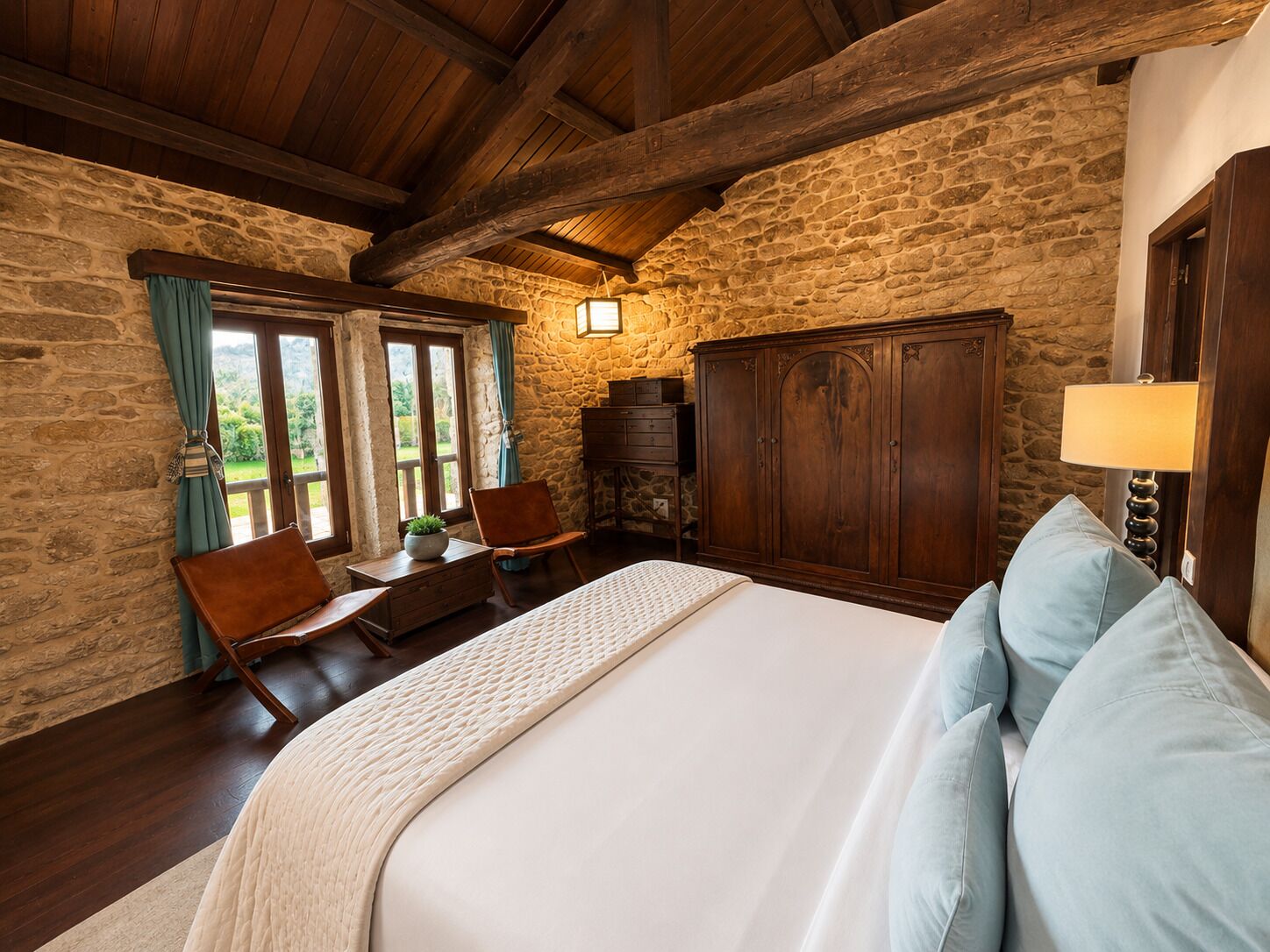 Une chambre avec un mur en pierre, des poutres en bois au plafond, un lit avec des oreillers, un bureau avec une chaise et une armoire.