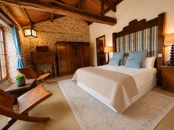 A bedroom with a stone wall, wooden beams, a bed with pillows, a nightstand, a lamp, and a chair.