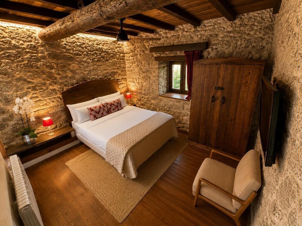Un dormitorio con pared de piedra, una cama de madera, una mesita de noche con lámpara, un armario de madera y una ventana con cortinas.