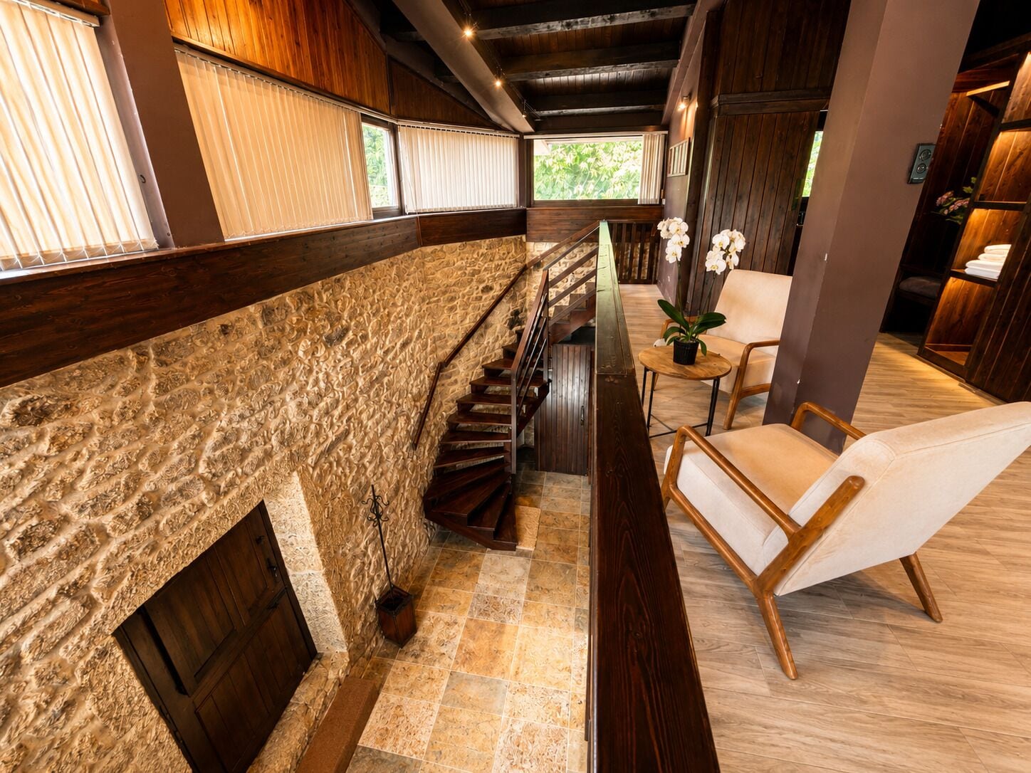 Un interior moderno con una pared de piedra, una escalera de madera y una zona de estar con una planta en maceta.