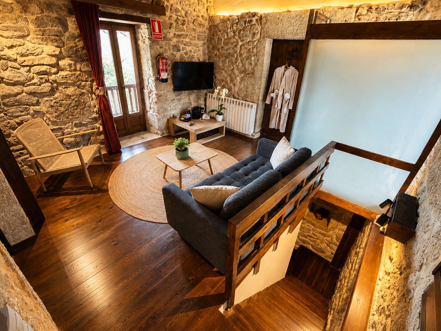 A cozy living room with a stone wall, a sofa, a wooden coffee table, a chair, and a television.