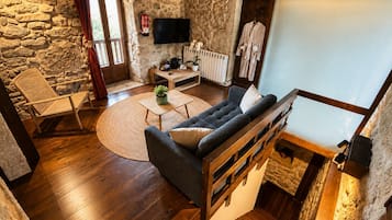 A cozy living room with a stone wall, a sofa, a wooden coffee table, a chair, and a television.