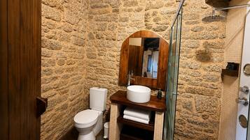 A bathroom with a stone wall, a wooden vanity, a white sink, a toilet, and a glass shower enclosure.