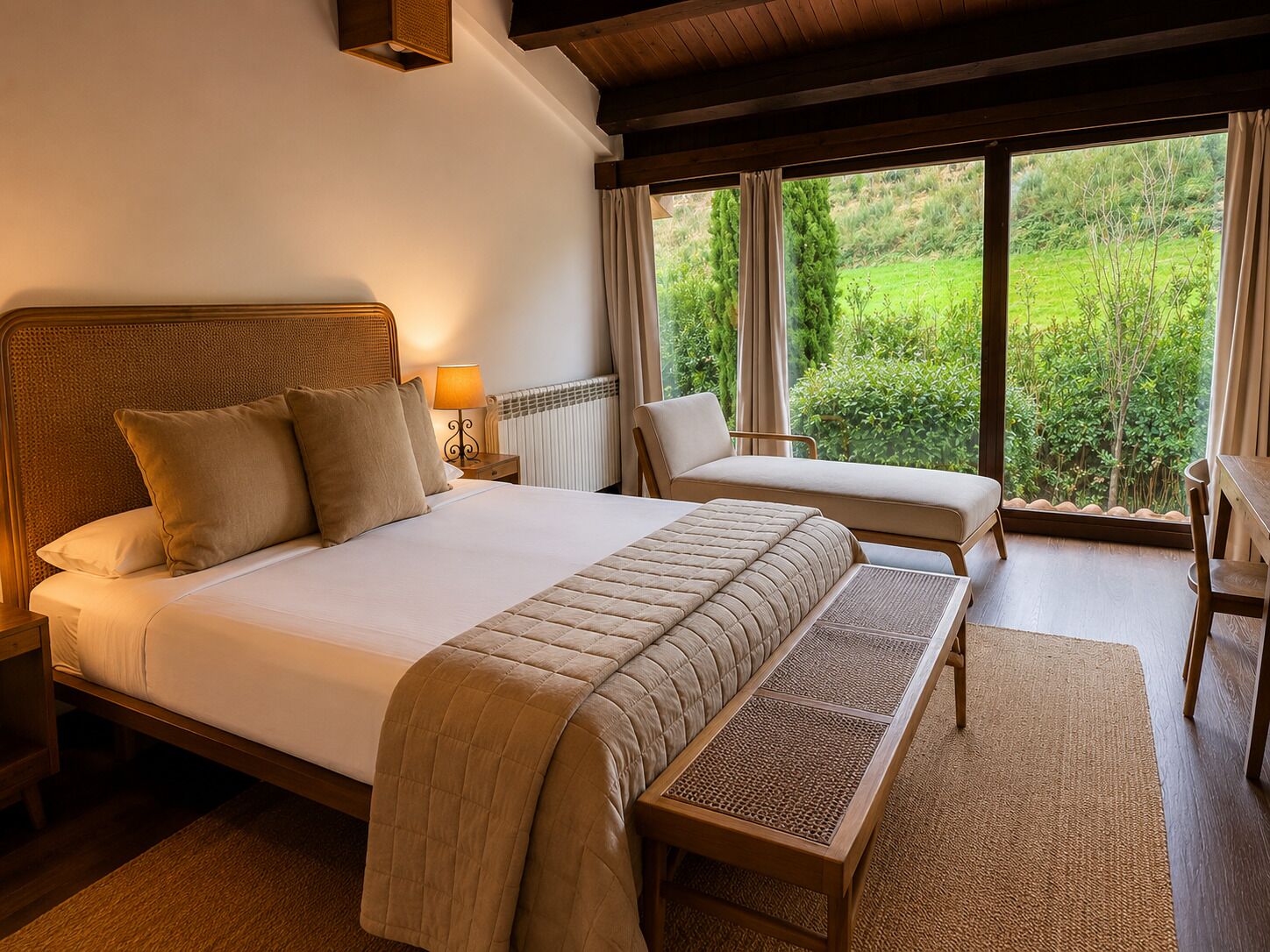 Een slaapkamer met een groot bed, een kleiner bed, een bankje, een tafel en uitzicht op groen buiten.