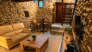 A cozy room with a stone wall, a wooden ceiling, a sofa, a coffee table, and a television.