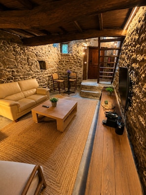 A cozy room with a stone wall, a wooden ceiling, a sofa, a coffee table, and a television.