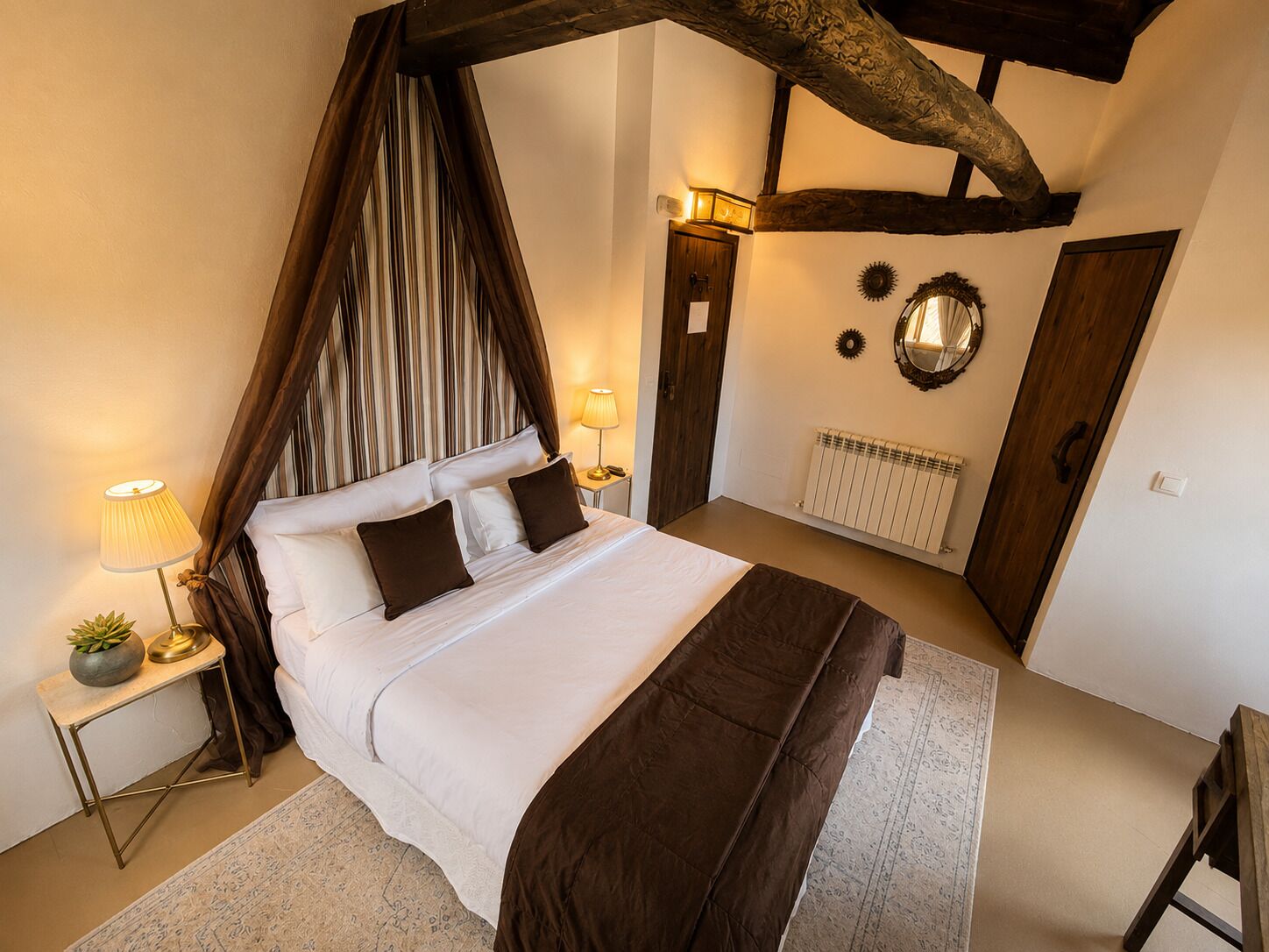 A bedroom with a four-poster bed, a bedside table with a lamp, a radiator, and a mirror on the wall.