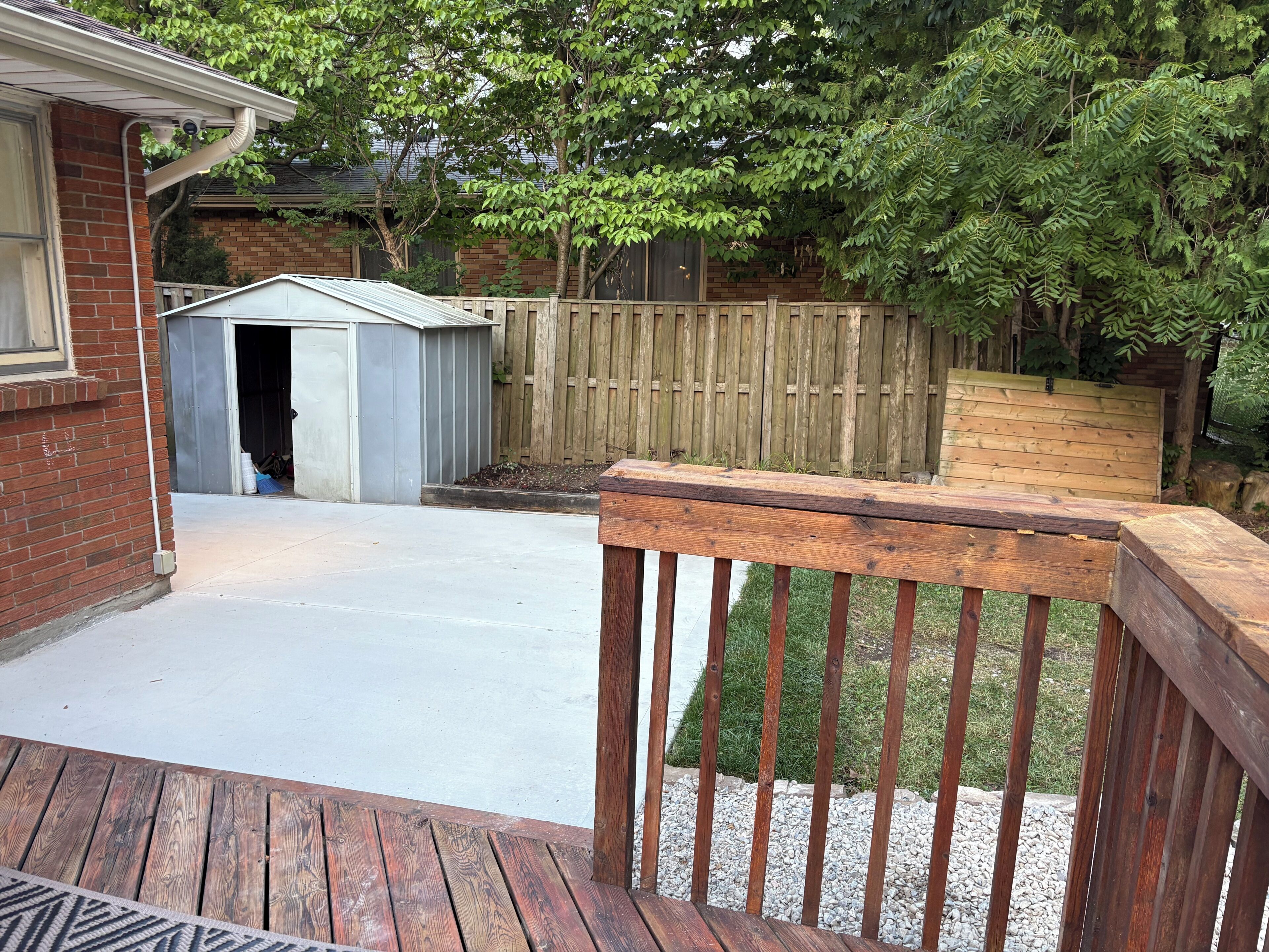Un jardin avec une terrasse en bois, un abri de jardin et une zone délimitée par une clôture.