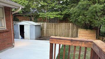 Un jardin avec une terrasse en bois, un abri de jardin et une zone délimitée par une clôture.