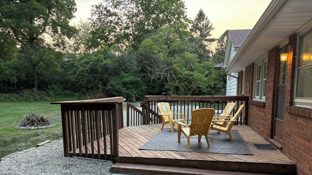 Eine Holzterrasse mit Adirondack-Stühlen und einem kleinen Tisch, umgeben von einem Ziegelhaus und einem Rasen.